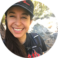 Mindy in a hat and t-shirt, with trees and rocks in the background